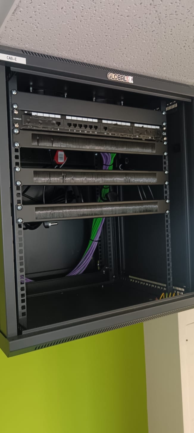Patch panels and horizontal cable managers, with purple and green cable runs inside a wall-mounted cabinet.